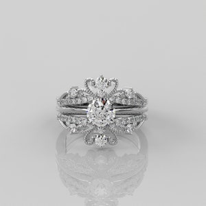 Pode incluir: Um anel de prata com um grande diamante redondo e claro cercado por diamantes menores. O anel tem um design delicado e ornamentado com um topo em forma de coroa.