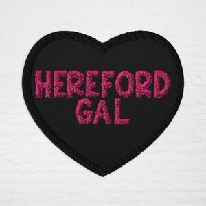 May include: Black heart-shaped patch with pink embroidered text that reads "HEREFORD GAL".