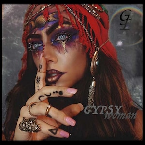 May include: A woman with dark hair and a red headscarf has intricate makeup on her face. She is wearing gold jewelry and has a ring on her finger. The text "GYPSY woman" is visible in the image.