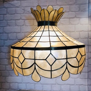 Op de afbeelding: Decoratieve hanglamp met een crèmekleurige, geometrisch patroon kap. De kap is zwart omlijnd en heeft een geschulpte onderrand. De bovenkant van de lamp heeft een kroonachtig ontwerp.