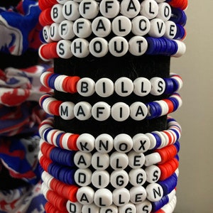 May include: A stack of colorful beaded bracelets with the words "LETS GO", "BUFFALO", "BUFFALOVE", "SHOUT", "BILLS", "MAFIA", "KNOX", "ALLE", "DIGGS", "ALLEN", "DIGGS", "KNOX", and "FAL" spelled out.