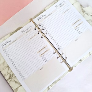 May include: A white planner with a marble pattern cover. The planner has a daily schedule, to-do list, and water intake and meal tracker sections. The planner is open to show the daily schedule and to-do list pages.