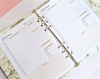 Op de afbeelding: Een witte planner met een marmerpatroon op de kaft. De planner heeft een dagschema, een to-dolijst en secties voor waterinname en maaltijdtracking. De planner is open om de pagina's van het dagschema en de to-dolijst te laten zien.