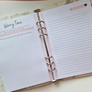 May include: A pink and white planner with a section labeled "Worry Time". The text reads "Worrying is a part of life, we have to worry but it doesn't have to be right now.  Down a 15 minute worry slot as part of your day.  Write down any worries which pop up throughout the day then revisit at a later time."