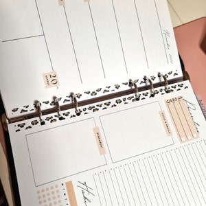 May include: A close-up of a weekly planner with a leopard print design. The planner has a section for daily tasks, a section for calls and emails, and a section for reminders. The planner also has a habit tracker with a grid of dots.