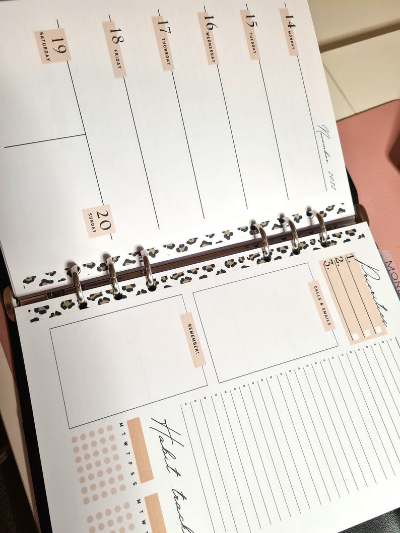 May include: A close-up of a weekly planner with a leopard print design. The planner has a section for daily tasks, a section for calls and emails, and a section for reminders. The planner also has a habit tracker with a grid of dots.