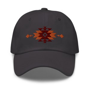 Op de afbeelding: Een donkergrijze baseballpet met een geborduurd geometrisch ontwerp in tinten oranje en rood.