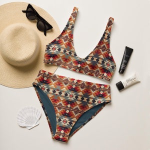May include: A two-piece swimsuit with a geometric pattern in shades of red, orange, blue, and beige. The top has a scoop neck and the bottom is high-waisted.
