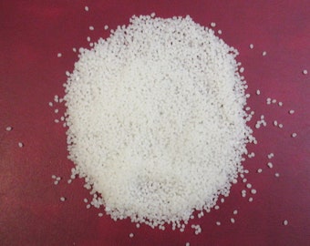 May include: A close-up image of a pile of small, white plastic pellets. The pellets are scattered on a red surface.