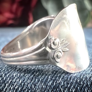 May include: A silver ring made from a repurposed spoon with a floral design. The ring is on a blue denim background.