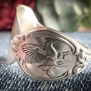 Può includere: Un anello d'argento realizzato da un cucchiaio riutilizzato con un design inciso di un uccello posato su un ramo.