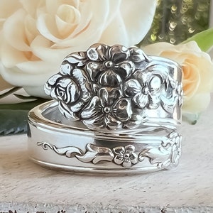 May include: A silver spoon ring with a floral design. The ring is made from a vintage spoon and features a delicate floral pattern.
