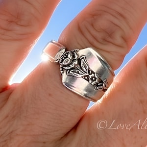 May include: A silver spoon ring with a floral design. The ring is worn on a finger with the sun shining through it.