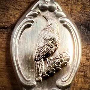 以下が含まれることがあります： 鳥が枝に止まっている装飾的なデザインが施された銀のスプーン。スプーンには、鳥と枝の細部までこだわった立体的なデザインが施されています。