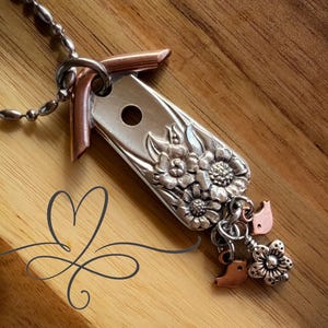 May include: A silver and copper birdhouse necklace with floral details and small bird charms.