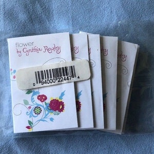 May include: A stack of five white gift tags with a floral design and the text "flower by Cynthia Rowley" and a barcode.