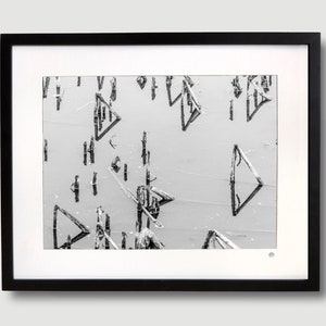 Op de afbeelding: Zwart-witfoto van een houten pier met driehoekige vormen die in het water worden weerspiegeld.