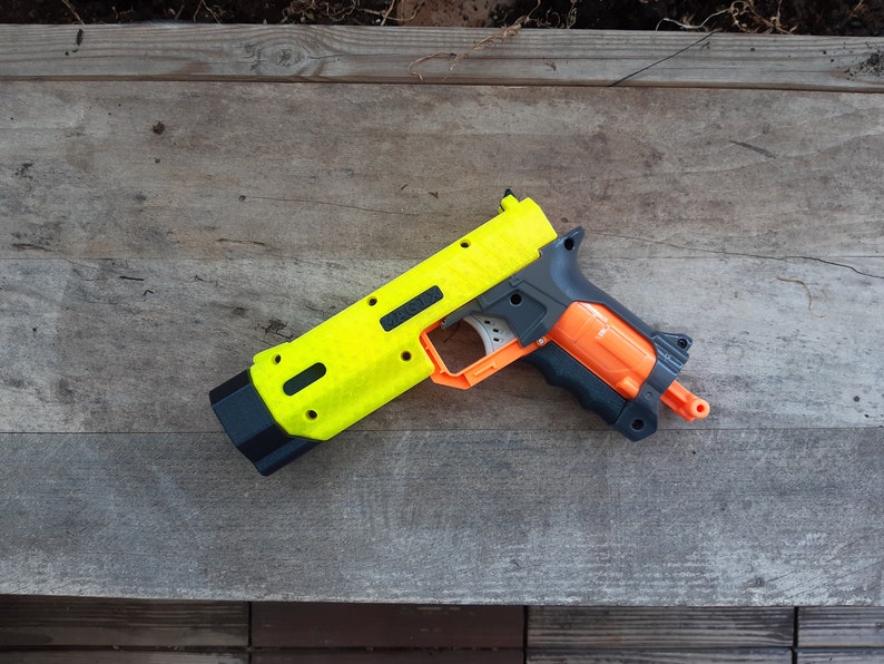 May include: A neon yellow and black toy gun with orange and gray accents. The toy gun is lying on a weathered wooden surface. The gun has a textured surface and a black handle.