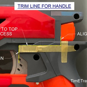 May include: Close-up of a red and gray toy gun with orange accents. The image includes text that reads "TRIM LINE FOR HANDLE" and "ALIGN". Yellow tape is used to mark alignment points. The image is a detailed guide for assembly or modification.
