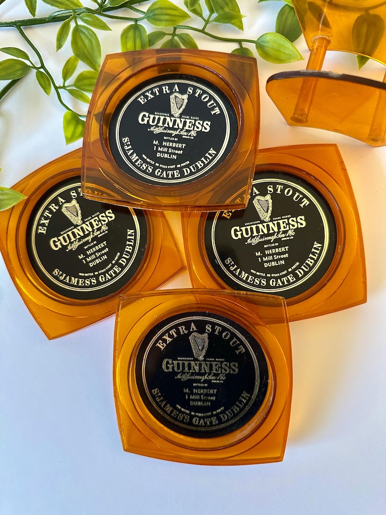 Peut inclure: Quatre dessous de verre carr&eacute;s ambr&eacute;s Guinness. Chaque dessous de verre pr&eacute;sente un centre circulaire noir avec le logo Guinness, les mots "Extra Stout" et "St. James's Gate Dublin" en lettres blanches. Les dessous de verre sont en plastique transparent.