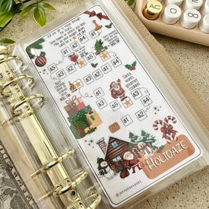 Könnte beinhalten: Eine transparente Kunststoff-Einlage für einen Ordner mit einem aufgedruckten weihnachtlichen Spar-Challenge-Spielbrett namens Holidaze. Das Brett enthält Illustrationen von Santa, einem Schneemann, Geschenken und Zuckerstangen.