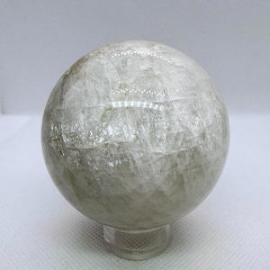 May include: A translucent, spherical crystal ball with a light green hue. The sphere sits on a clear, round base. The surface of the ball has a textured appearance.