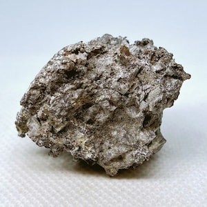 May include: A close-up of a rough, irregularly shaped rock. The rock has a mix of gray, brown, and white colors, with a textured surface. The rock appears to be a mineral specimen.