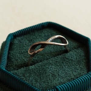 Op de afbeelding: Een zilveren oneindigheidsring in een groene fluwelen ringendoos.