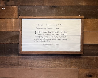 May include: A framed white sign with black text that reads "St-p! ft-p! ft-p! Noi Tuesday-Morning, December 17, 1765. THE True-born Sons of Li-berry, are deftred to meet under LIBERTY-TREE, at XII 'Clock, THIS DAY to hear the the public Refignation, under Oath, of ANDREW OLIVER, Efs, Diftributor of Stamps for the Province of the Moffachusetts-Bay. A Refignation? YES."