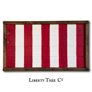 May include: A wooden sign with red and white stripes painted on it. The sign is framed with a dark brown wood frame. The sign has the text "LIBERTY TREE CO." printed on the bottom.