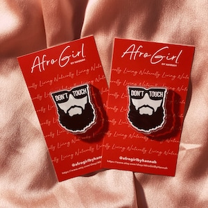 May include: Two red cards with white text that reads "Afro Girl by Hannah" and a black and white illustration of a face with a beard and sunglasses. The text on the illustration reads "Don't Touch".