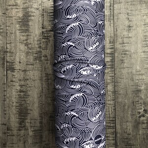 May include: A black and white patterned neck gaiter with a wave design. The gaiter is rolled up and has a small black circle with the word "nekku" printed on it.