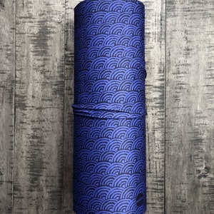 May include: A blue and black fabric tube with a repeating pattern of stylized waves. The fabric tube is rolled up and has a small black circle with white text on the side.