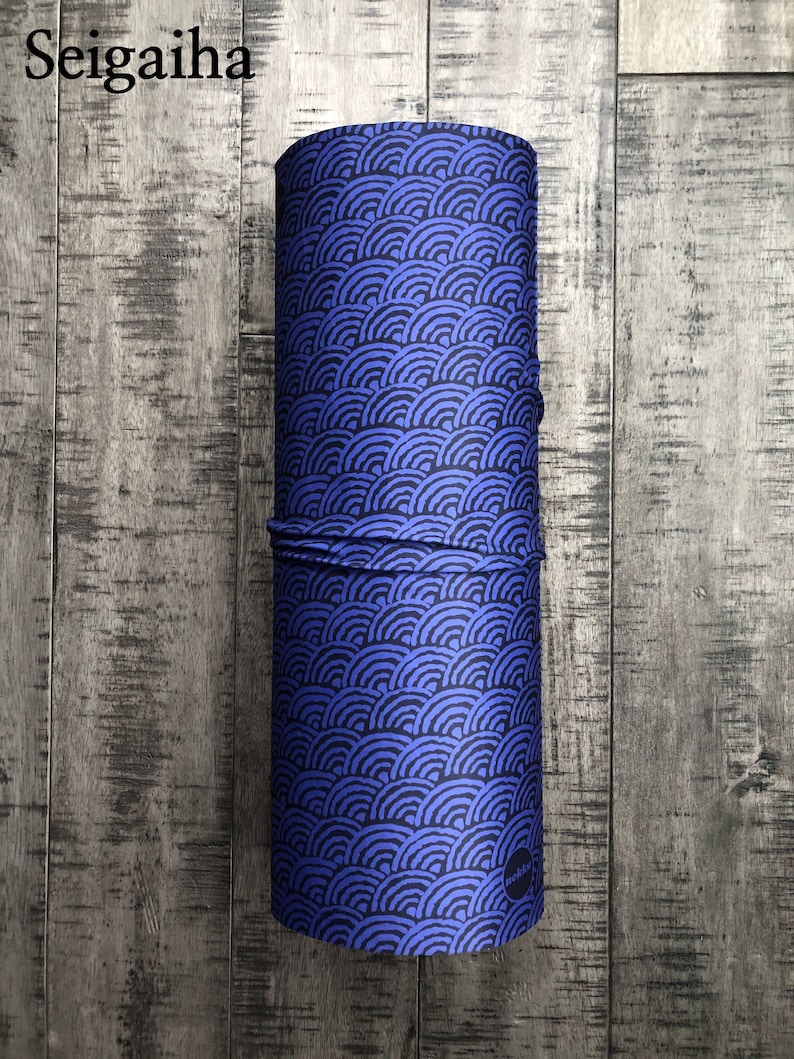 May include: A blue and black fabric tube with a repeating pattern of stylized waves. The fabric tube is rolled up and has a small black circle with white text on the side.