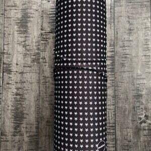 May include: A black and white patterned neck gaiter with a white "nekkw" logo. The gaiter is rolled up and sitting on a wooden surface.