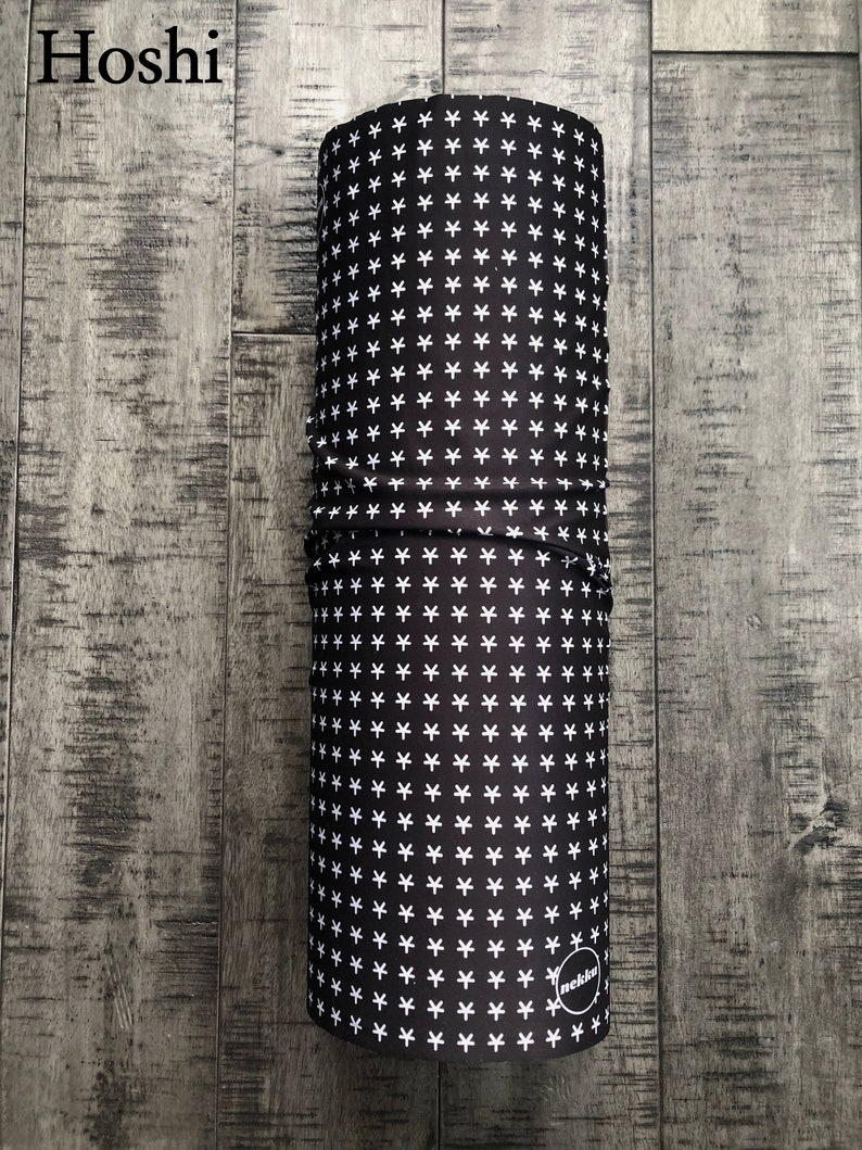 May include: A black and white patterned neck gaiter with a white "nekkw" logo. The gaiter is rolled up and sitting on a wooden surface.