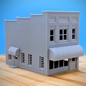 Peut inclure: Un modèle gris d'un bâtiment à deux étages avec une façade en briques, un auvent et plusieurs fenêtres. Le bâtiment présente un design détaillé, comprenant une petite porte et un sommet décoratif. Le modèle est posé sur un fond bleu.