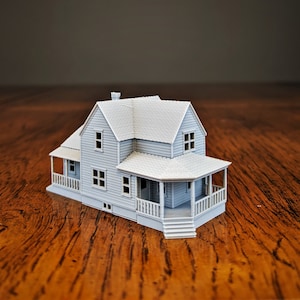May include: A white model house with a porch and a gabled roof. The house is made of plastic and has a realistic appearance.