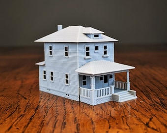 Może przedstawiać: Jasnoniebieski model miniaturowego domu z werandą, dwoma piętrami i dwuspadowym dachem. Model ma wiele okien i komin. Dom stoi na drewnianej powierzchni.