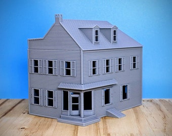 Op de afbeelding: Een grijs model van een huis met twee verdiepingen, een veranda en een kleine helling. Het huis heeft meerdere ramen en een dak met twee dakkapellen.