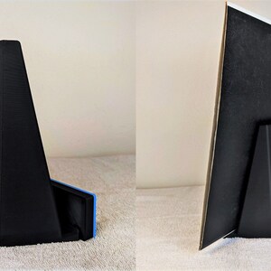 May include: A black plastic stand with a triangular base and a rectangular back panel. The stand has a small hole in the back panel for hanging. The stand is designed to hold a picture or other object.