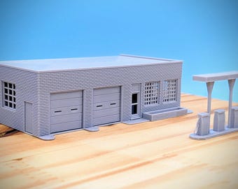 May include: A gray model of a brick building with two garage doors and a gas station pump. The building has windows and a small awning. The gas station pump has a canopy and two pumps.