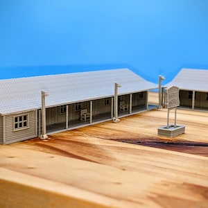 Puede incluir: Un modelo 3D impreso de un motel con un letrero que dice "Lariat Motel". El modelo está hecho de plástico gris y está colocado sobre una superficie de madera.