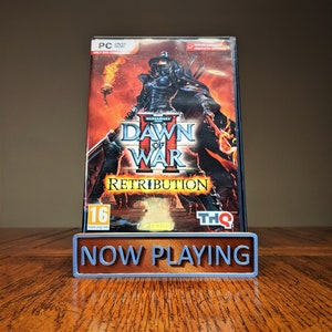May include: A video game case for Warhammer 40,000: Dawn of War II - Retribution. The case is red, black, and white with a picture of a space marine on the front. The game is rated 16+ by PEGI.