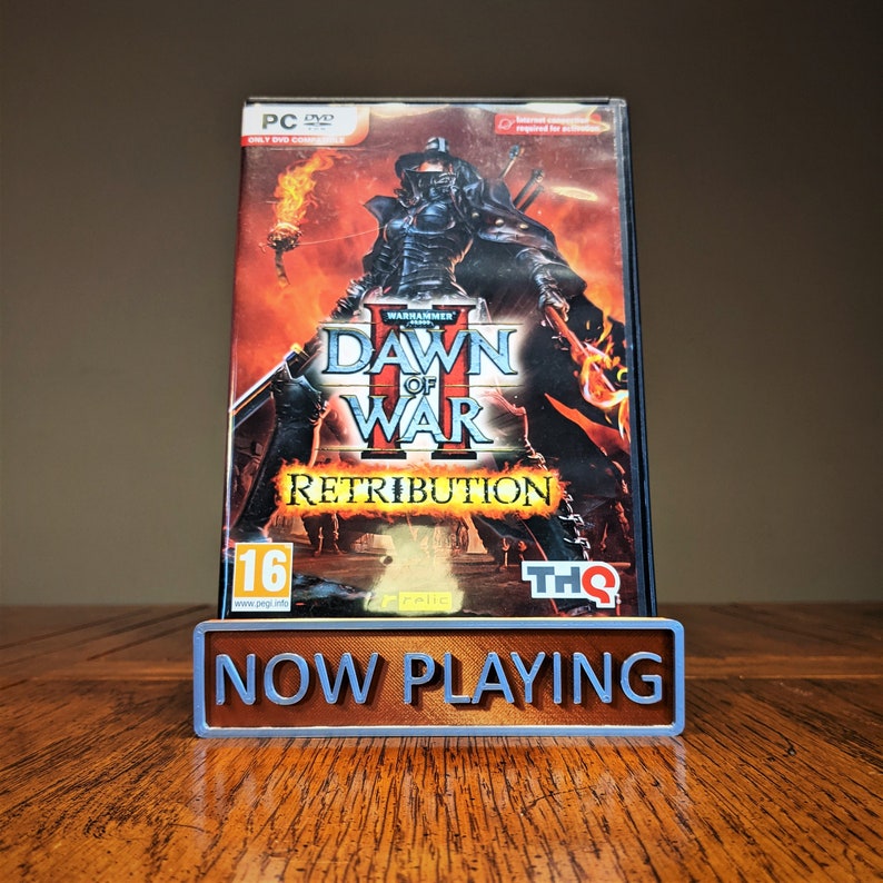 May include: A video game case for Warhammer 40,000: Dawn of War II - Retribution. The case is red, black, and white with a picture of a space marine on the front. The game is rated 16+ by PEGI.