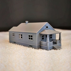 May include: A gray 3D printed model of a small house with a porch and steps. The house has a gabled roof, a chimney, and several windows.