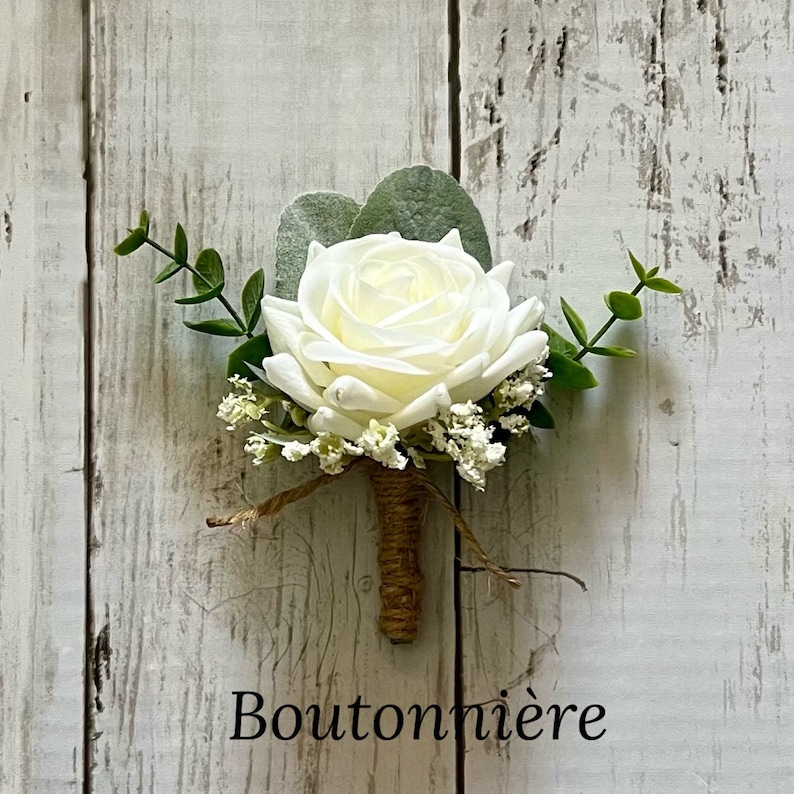 May include: A boutonniere featuring a single cream-colored rose, accented with small white baby's breath flowers, green eucalyptus leaves, and a dusty miller leaf. The stem is wrapped in brown twine, and the word Boutonni&egrave;re is printed below.