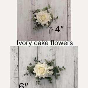K&ouml;nnte beinhalten: Zwei elfenbeinfarbene Tortenblumen-Gestecke mit wei&szlig;en Rosen und gr&uuml;nem Eukalyptuslaub. Das obere Gesteck ist mit 4 Zoll gekennzeichnet, das untere mit 6 Zoll. Der Text Ivory cake flowers steht mittig zwischen den beiden Gestecken.