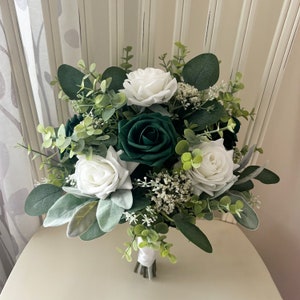 May include: A bridal bouquet with white roses and dark green roses, accented with greenery.
