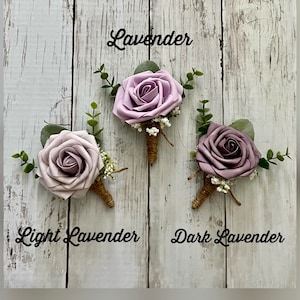 Op de afbeelding: Drie florale corsages met rozen in de tinten lavendel, lichtlavendel en donkerlavendel. Elke roos is versierd met groene eucalyptusbladeren, witte gipskruid en een steel omwikkeld met bruin touw. De tekstlabels vermelden Lavender, Light Lavender en Dark Lavender.